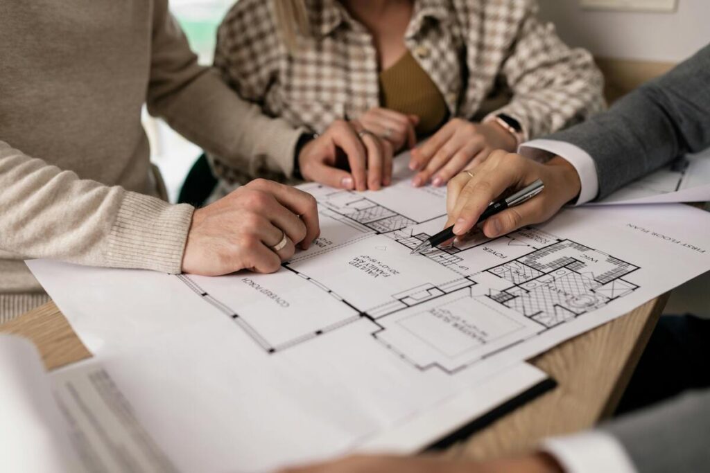 Projeto imobiliário sendo analisado por três pessoas. Com a Selic alta, empréstimos e financiamentos ficam mais caros.